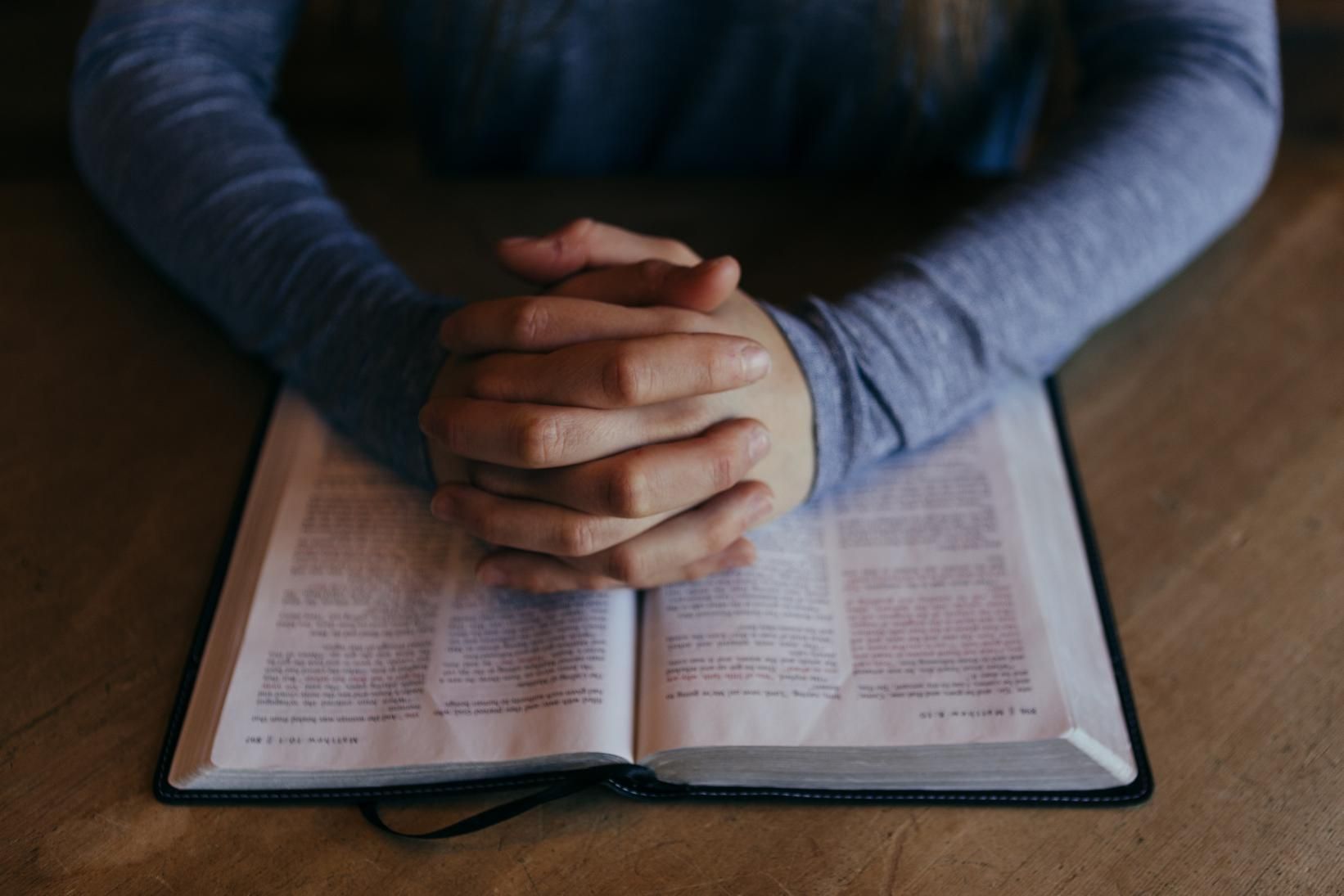 Una persona con sus manos cruzadas encima de un libro sagrado.
