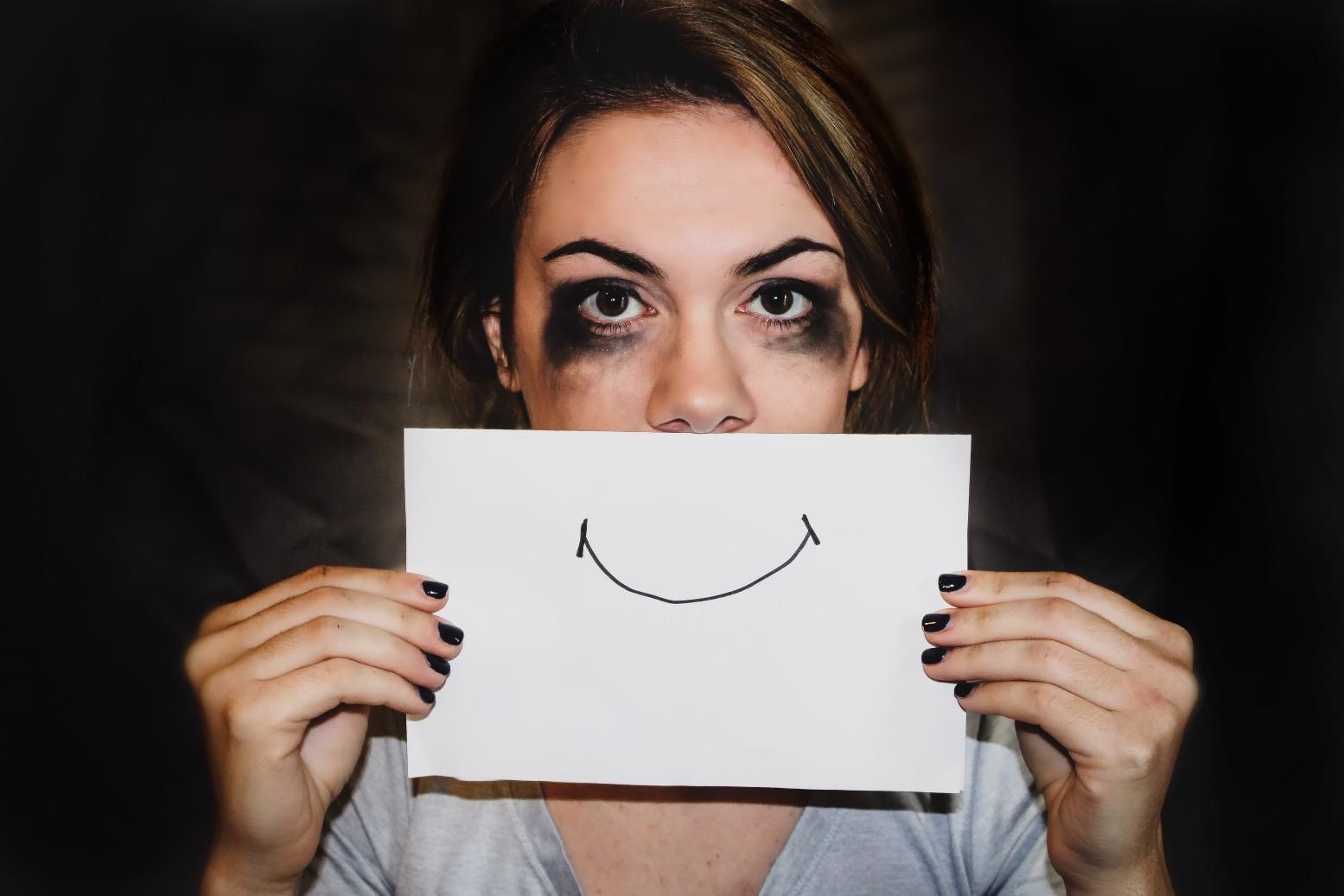 Una mujer con una papel con una sonrisa sobre su cara triste. Representa el abuso.